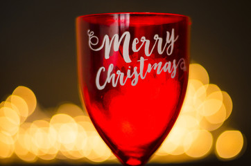 Red wineglass with Merry Christmas phrase on bokeh background