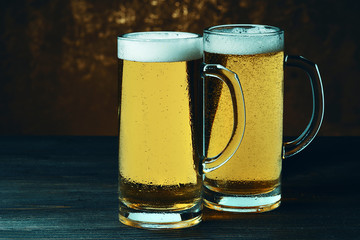 Two mugs of beer on a dark background.