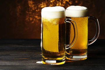 Two mugs of beer on a dark background.