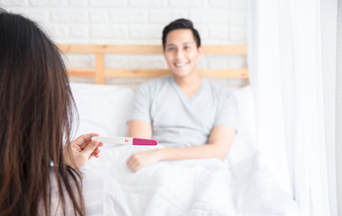 Selective focus Pregnancy test positive result on hand of smiling woman in her bedroom,Blurred background of her glad couple on the bed.