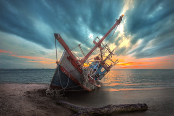 an old useless fishing boat laying dead on the sea beach at sunset scenery in background
