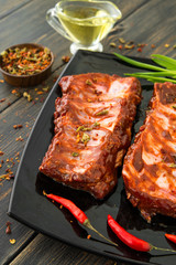 A black glass plate of juicy smoked spareribs with red peppers, green onion and olive oil