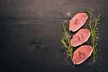 Raw meat. Beef steak with rosemary and spices on a black wooden background. Top view. Free space for text.