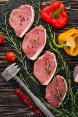 Beef steak with fresh vegetables and rosemary and spices on a black wooden background. Top view. Free space for text.