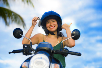 Obraz premium pretty Asian Chinese girl showing key of new motorbike wearing motorcycle safety helmet smiling proud in scooter buying and rental