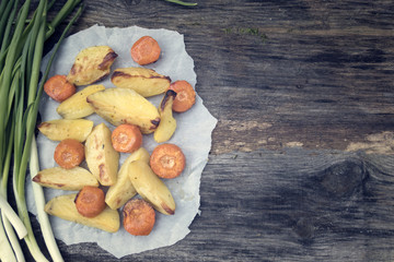 Rustic potatoes, green onions and baked carrots on a wooden table and copy space.