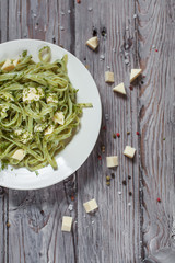 spaghetti with spinach green with mozzarella, herbs on a white plate on a light wooden table