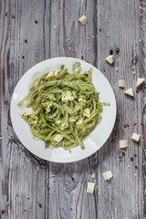 spaghetti with spinach green with mozzarella, herbs on a white plate on a light wooden table
