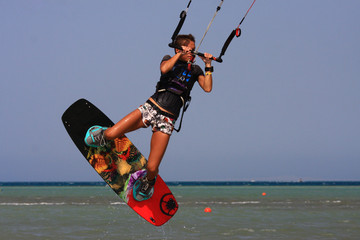 Kitesurfing girl in boots and shorts with kite in blue sky on kiteboard in the blue sea jumping air trick. Recreational activity, water sports, action, hobby and fun in summer time. Kiteboarding sport © yanamavlyutova