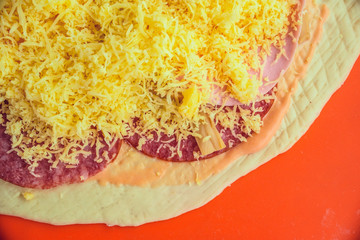 raw pizza with cheese and mushrooms on a red background