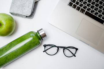 Healthy working life style. Laptop with stationery and green smoothies with apple on white table. Top view, flat lay