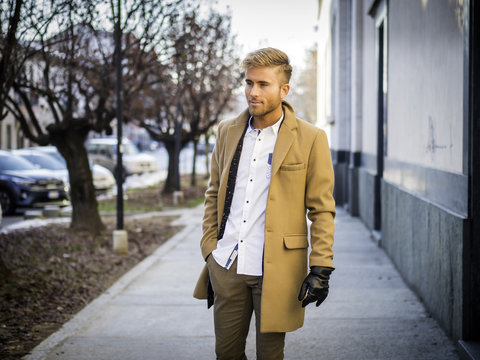 Handsome trendy blond man standing outdoor in European city setting with elegant old historic building behind