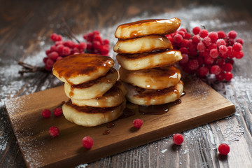 syrups with powdered sugar on a wooden cutting board, a sieve of a viburnum berry and caramel topping on a dark wooden table