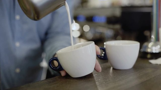 Pouring stream milk into a cup of espresso. 4K