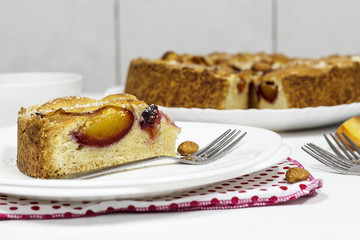 Homemade pie with almond frangipan and organic plums on white plate. Light background. Selective focus.