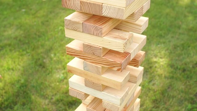 Jenga tower of large wooden bars in the Park on the grass. Big Games outdoors. Game jenga. Close-up. Slow motion.