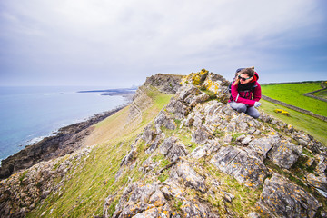 Female Backpacker Looking Into Distance At Rocky Sea Shore In Rhossili, Wales Coast Path