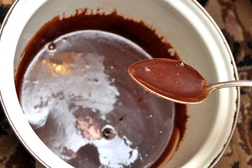 Tasty melted chocolate in a spoon and a white saucepan.