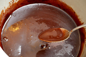 Tasty melted chocolate in a spoon and a white saucepan.