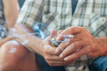 Close up of an old man hands holding mobile phone and cigarette with smoke.