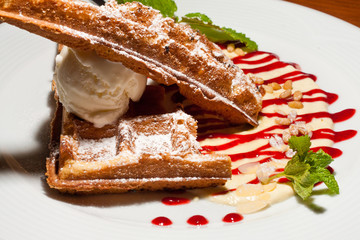 Close-up of a fresh Belgian waffle on a plate in a restaurant with topping, caramel, mint and ice cream ball, sweet dessert.