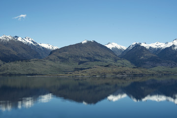 Fototapeta premium Paisaje de montañas frente a un gran lago donde se reflejan. Cielo azul despejado.