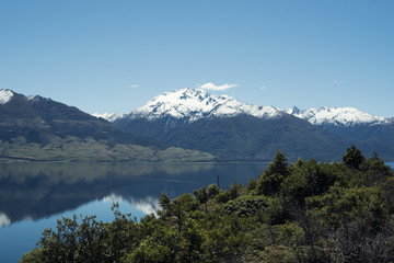 Fototapeta na wymiar Paisaje de montañas frente a un gran lago donde se reflejan. Cielo azul despejado.