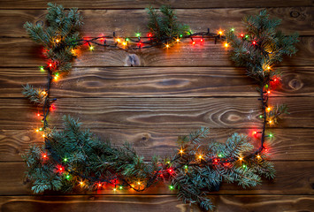 Christmas frame with snow on wood background with luminous garland and pine branches