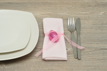 A place setting for easter consisting of plates, a knife and fork with a napkin tied with a pink bow with a wrapped easter egg