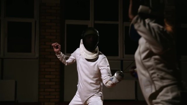 Young man and woman in hats and costumes for fencing battle on the foil. Dark background.
