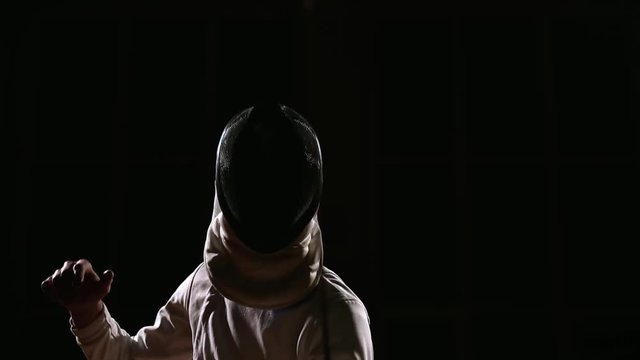 A man dressed for fencing wears a mask and is preparing a rapier. Close-up. Portrait