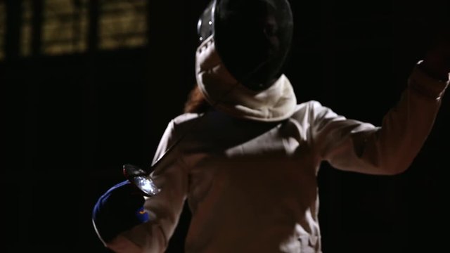 Close-up of a girl dressed in a suit and a fencing mask makes a sword and becomes a rack