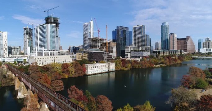 A slow reverse aerial establishing shot of the Austin, Texas city skyline on a sunny late Autumn day. Railroad bridge and Colorado River in the foreground.	