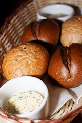 Assorted bread rolls in a wicker basket with sauce and butter in a close-up restaurant.