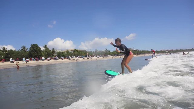 Young girl surfing in the ocean and having fun. Teenage girl in a surfing on the beah Kuta in Bali. Surfer with surf board. Lifestyle, people water sport adventure camp, beach extreme swim on summer