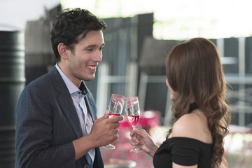 Portrait of smiling young man and woman talking while holding red sparkling wine glass. Pretty single girl flirting with young handsome man in a real bar scene, trying to take her home. Party concept.