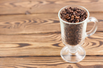 Lot of fried coffee beans in transparent glass for mulled wine with handle and leg on old wooden rustic brown planks