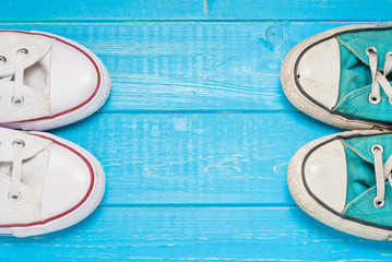 Top view of the a pair of new and old sneakers opposite each other, the concept of transferring experience and changing generations, hipster shoes on a wooden background