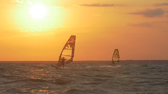 Two windsurfers on the sea at sunset