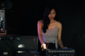 Fototapeta na wymiar Woman DJ party concept. Young Chinese woman DJ mixing music on colorful background listening to her music. Selective focus with blurred background.