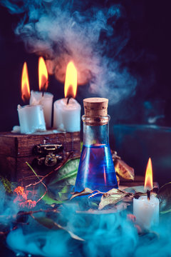 Magical still life with spells, herbs, potion ingredients, wax candles and a glass bottle with mystic liquid on a dark background. Modern witchcraft concept with copy space.