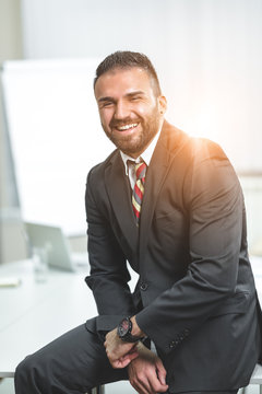 Portrait of happy smiling young businessman.He is sitting at a desk in his office.