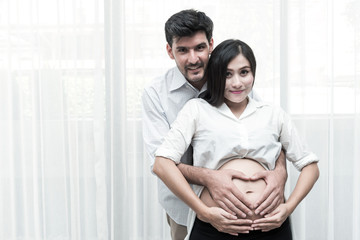 Mixed race parenthood concept. Portrait of young Chinese pregnant and her white male husband holding each other. Taken indoor with real six months old pregnant woman.