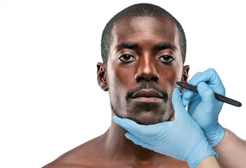 Surgeon drawing marks on male face against gray background. Plastic surgery concept