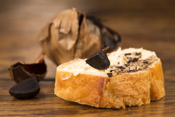 Black garlic on bread on an old wooden table