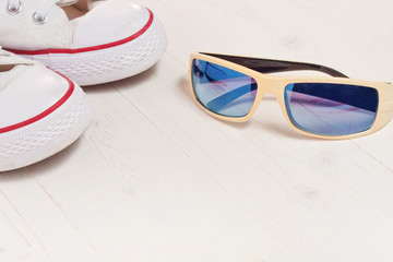 A pair of new white hipster sneakers with sunglasses next to an old wooden background, a casual...