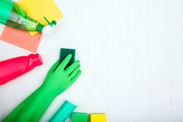 Cleaning products and hand in rubber gloves on white wooden background with empty space, top view
