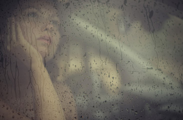 Sad woman looking through the window with rain drop in the car. Face of young female behind rain...