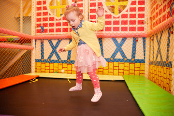 Happy little kid girl play in the playing room jumping on the batute trampoline. Funny child having fun indoors. Birthday party