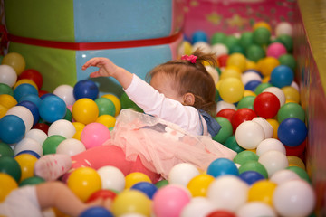 Fototapeta na wymiar Happy little kid girl play in the playing room pool full of colorful balls. Funny child having fun indoors. Birthday party